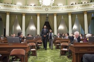 A speaker addressing an audience seated in a legislative chamber.